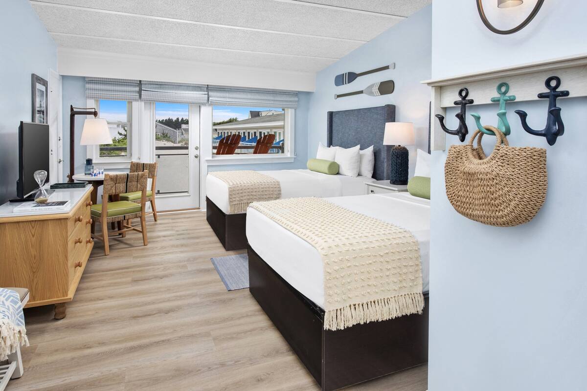 Ein Hotelzimmer mit zwei Betten, einem Schreibtisch, einem Stuhl und Blick auf den Strand.