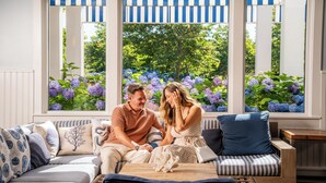 A couple sitting on a striped sofa with a view of purple hydrangeas through large windows.