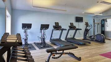 Een sportschool met loopbanden, elliptische trainers en een zone voor bankdrukken.