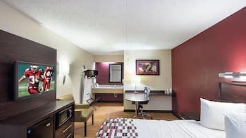 A hotel room with a bed, a desk, a chair, a television, and a bathroom.