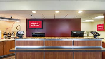 Un comptoir d’accueil équipé d’un téléviseur à écran plat affichant le message « Wi-Fi gratuit dans toutes les chambres » et d’un ordinateur Lenovo.