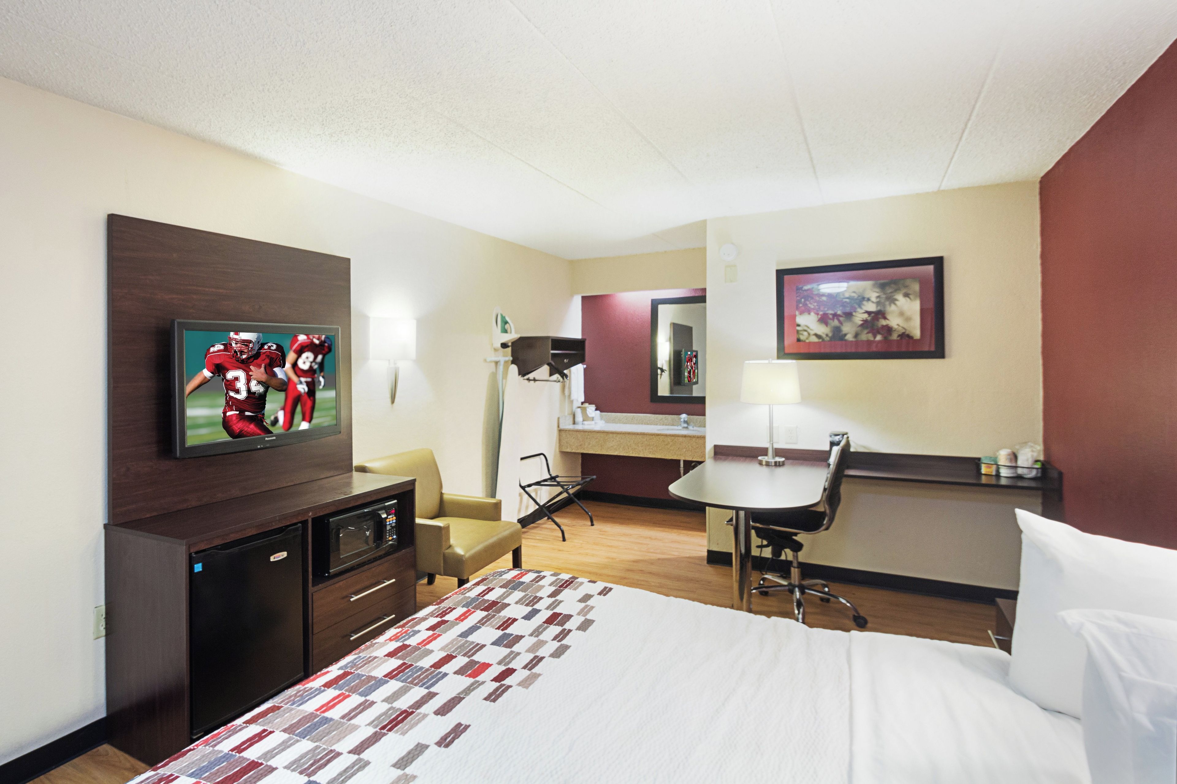 A hotel room with a bed, a desk, a chair, a television, and a bathroom.