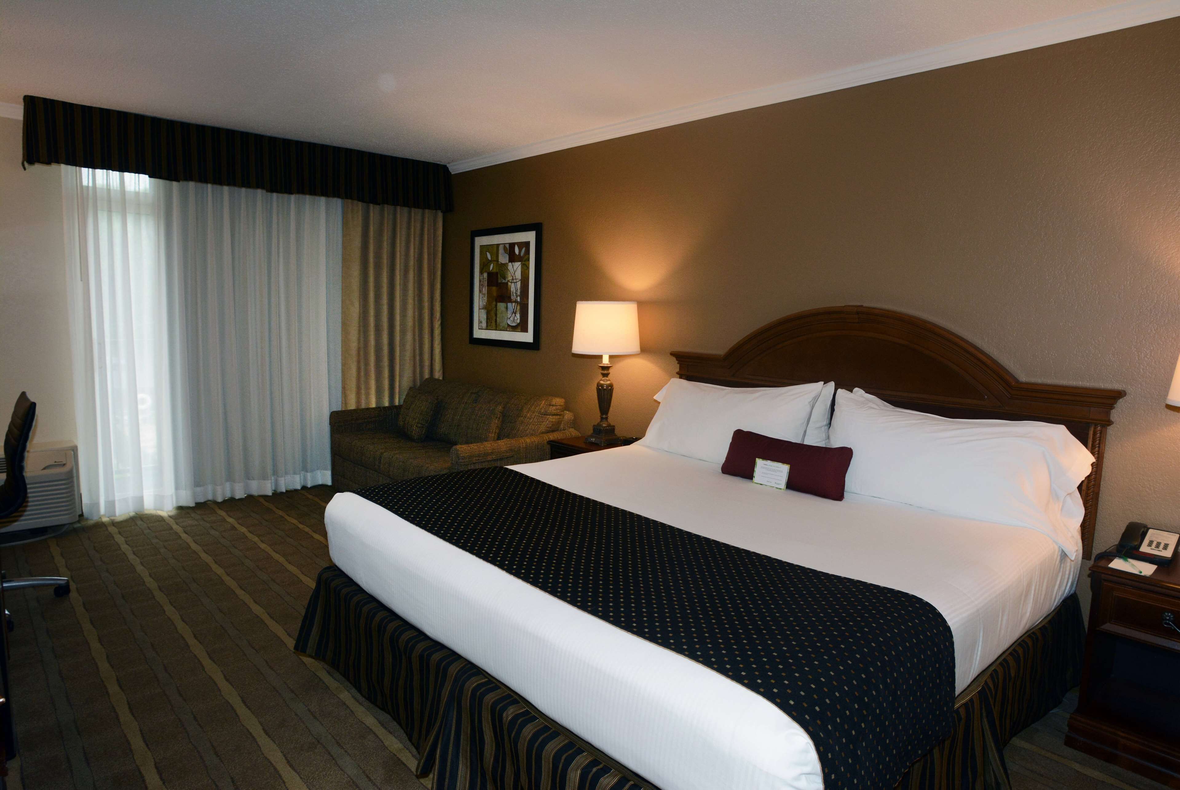 A hotel room with a large bed, a chair, a desk, and a lamp.