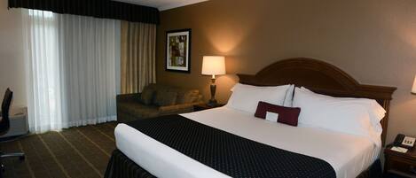 A hotel room with a large bed, a chair, a desk, and a lamp.