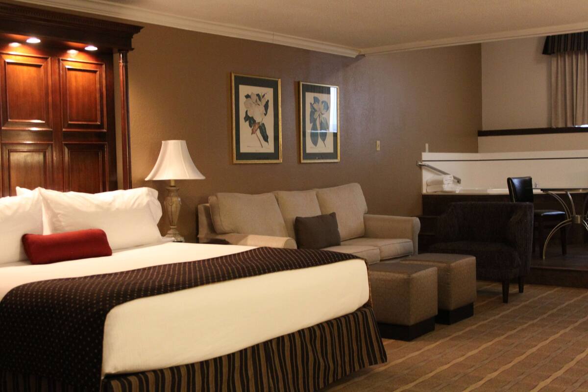 A hotel room with a large bed, a sofa, a chair, and a desk. There are two framed pictures on the wall.