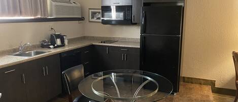 A compact kitchen with a round glass table, black chairs, a built-in microwave, and a black refrigerator.