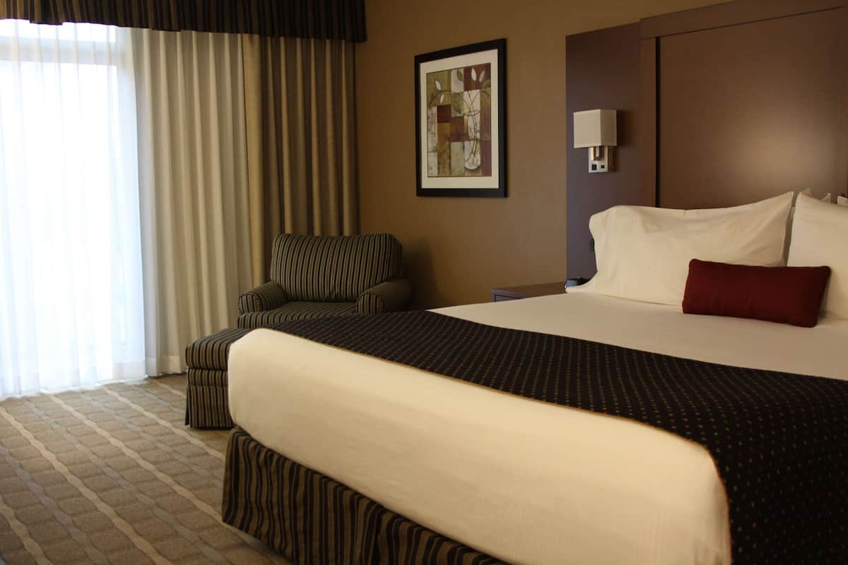 A hotel room with a large bed, a striped armchair, a nightstand, and a framed picture on the wall.