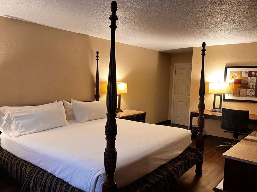 A four-poster bed with a wooden frame, a desk with a chair, and a painting on the wall.