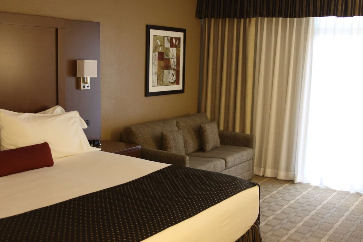 A hotel room with a large bed, a sofa, a wall-mounted lamp, and a framed picture.