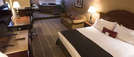 A hotel room with a bed, a desk, a chair, a sofa, a small table, a lamp, a painting, and a hot tub in the background.
