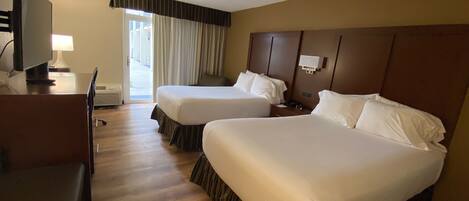 Habitación de hotel con dos camas, un escritorio, un televisor y una ventana con cortinas.