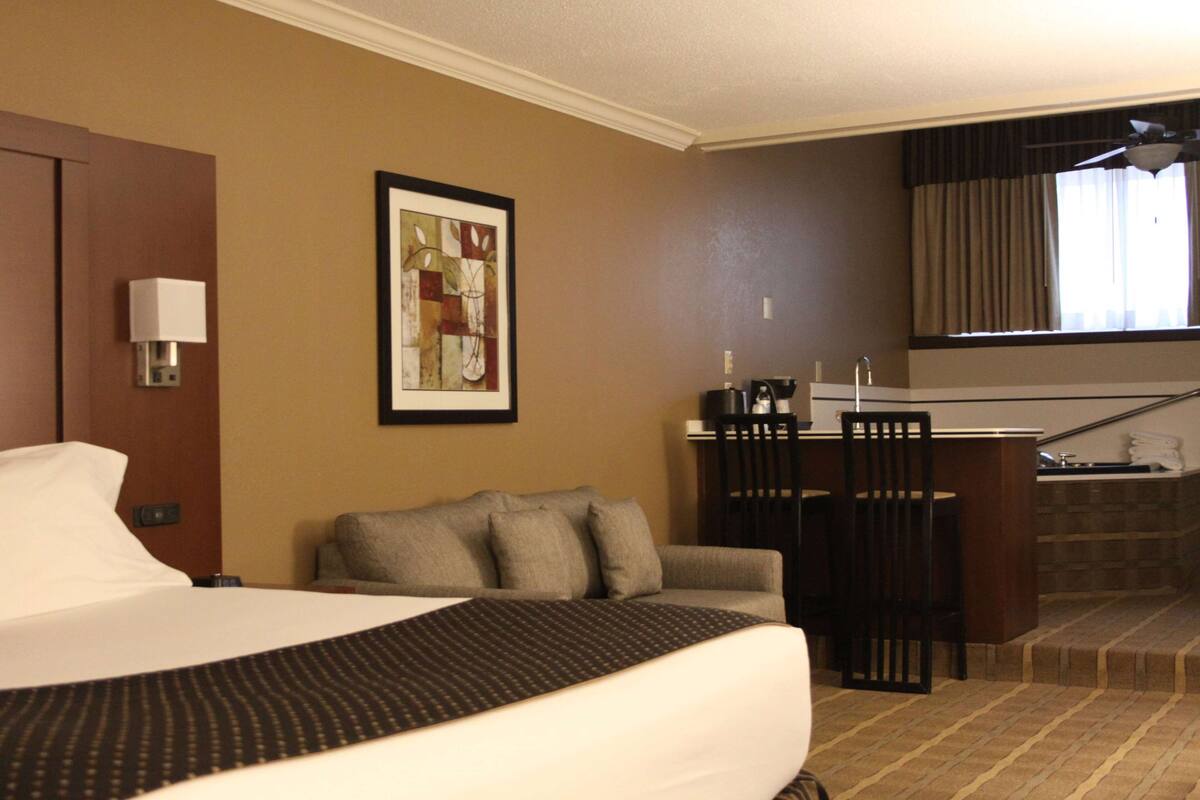 A hotel room with a bed, a sofa, a desk with a chair, a framed picture on the wall, and a window with curtains.