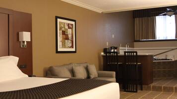 A hotel room with a bed, a sofa, a desk with a chair, a framed picture on the wall, and a window with curtains.
