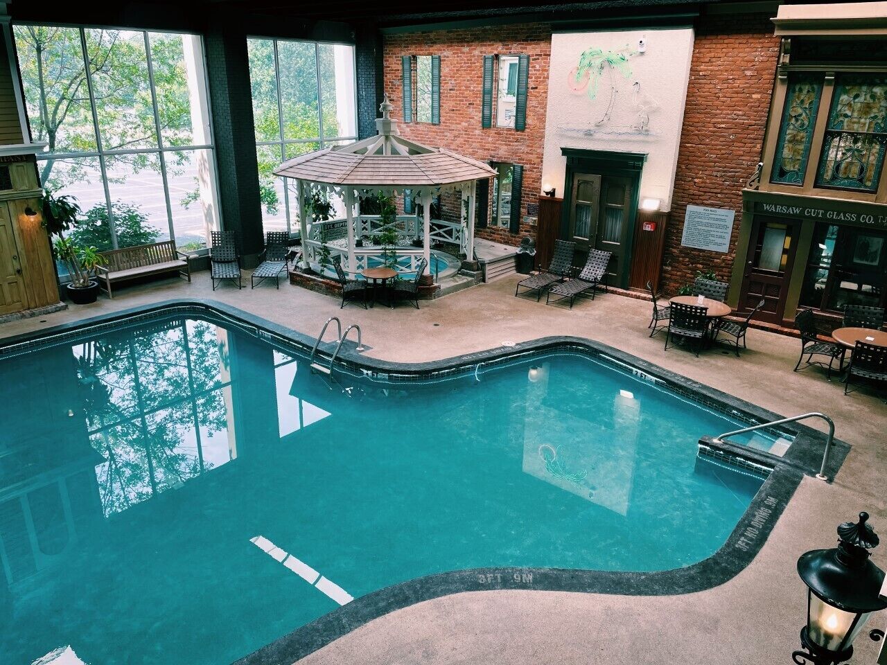 Una piscina interior con un pabellón, sillas de descanso y una pared de ladrillo con puerta de cristal.
