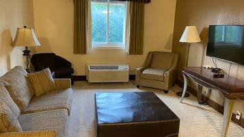 A hotel room with a sofa, two armchairs, a coffee table, a TV, and an air conditioning unit.