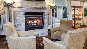 A cozy living room with a stone fireplace, two armchairs, and a glass cabinet with decorative items. - Wyndham Garden Warsaw (Warsaw)