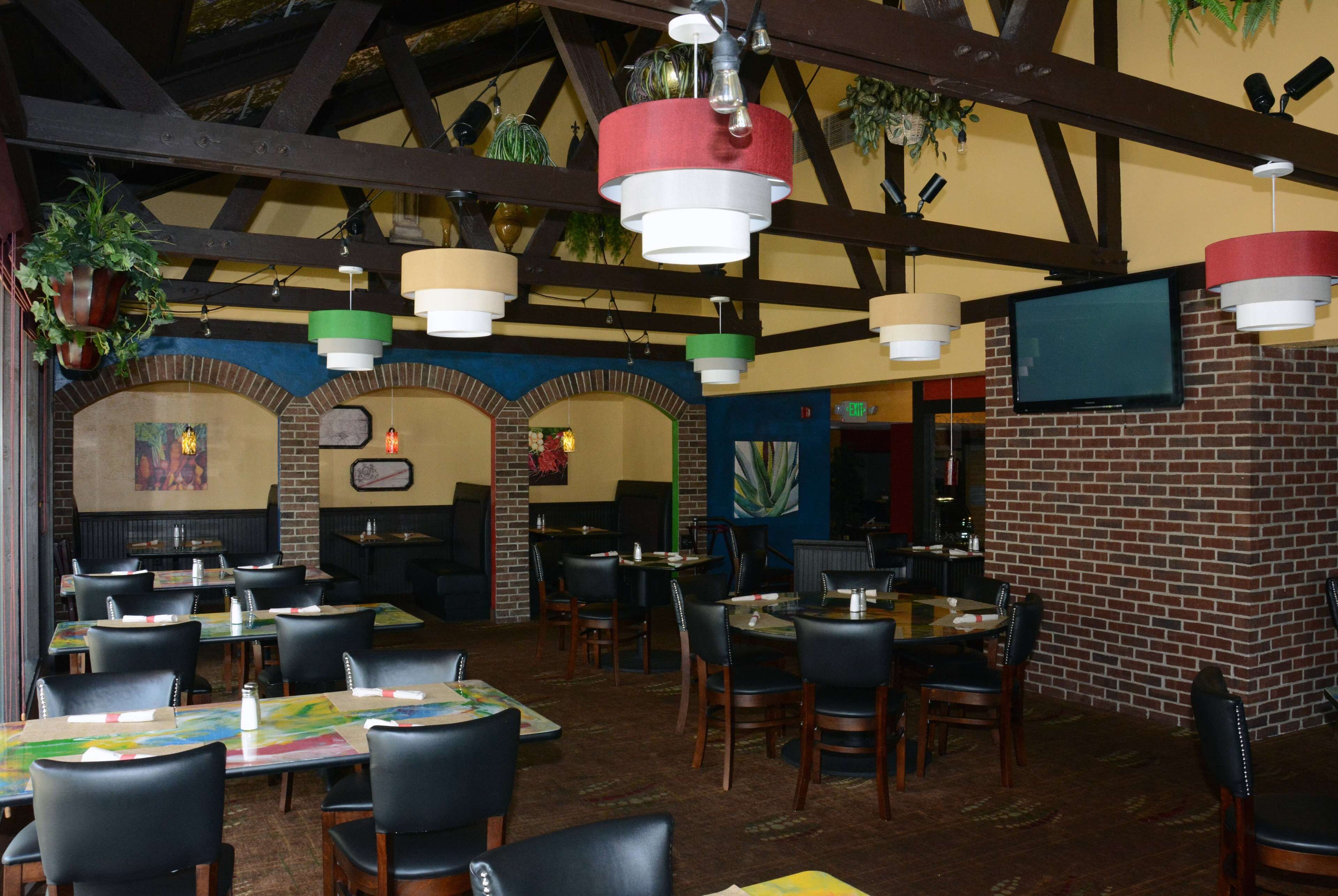 A restaurant with brick walls, wooden beams, and hanging pendant lights. Tables and chairs are arranged for dining.
