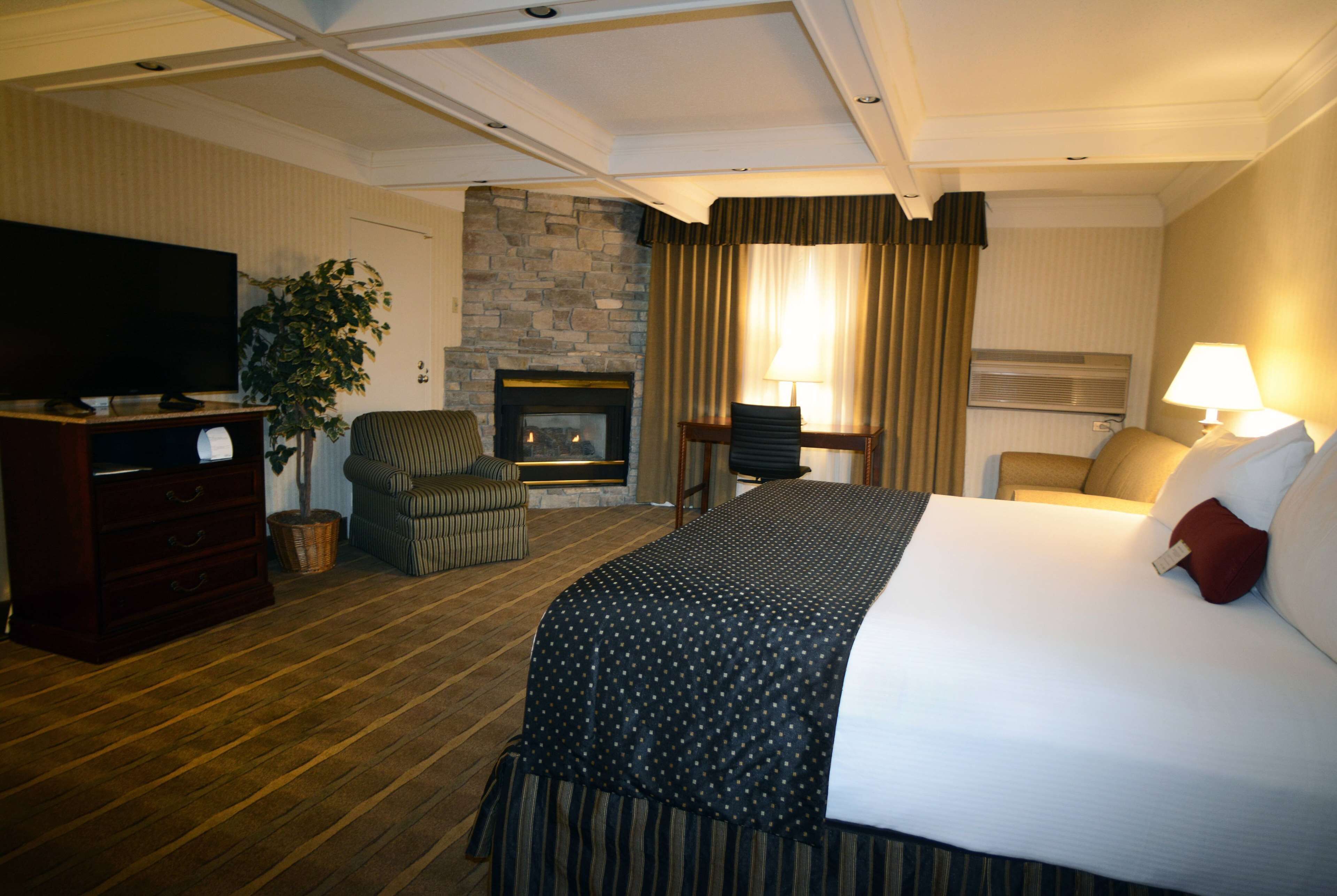 Una habitación de hotel con una cama grande, televisión, chimenea, una silla y un escritorio.