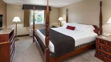 A four-poster bed with a wooden frame, a television on a dresser, and a desk lamp.