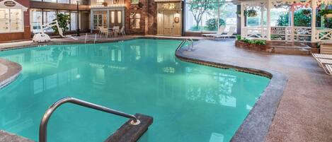 An indoor swimming pool with a stone border, a gazebo, and a view of the outside.