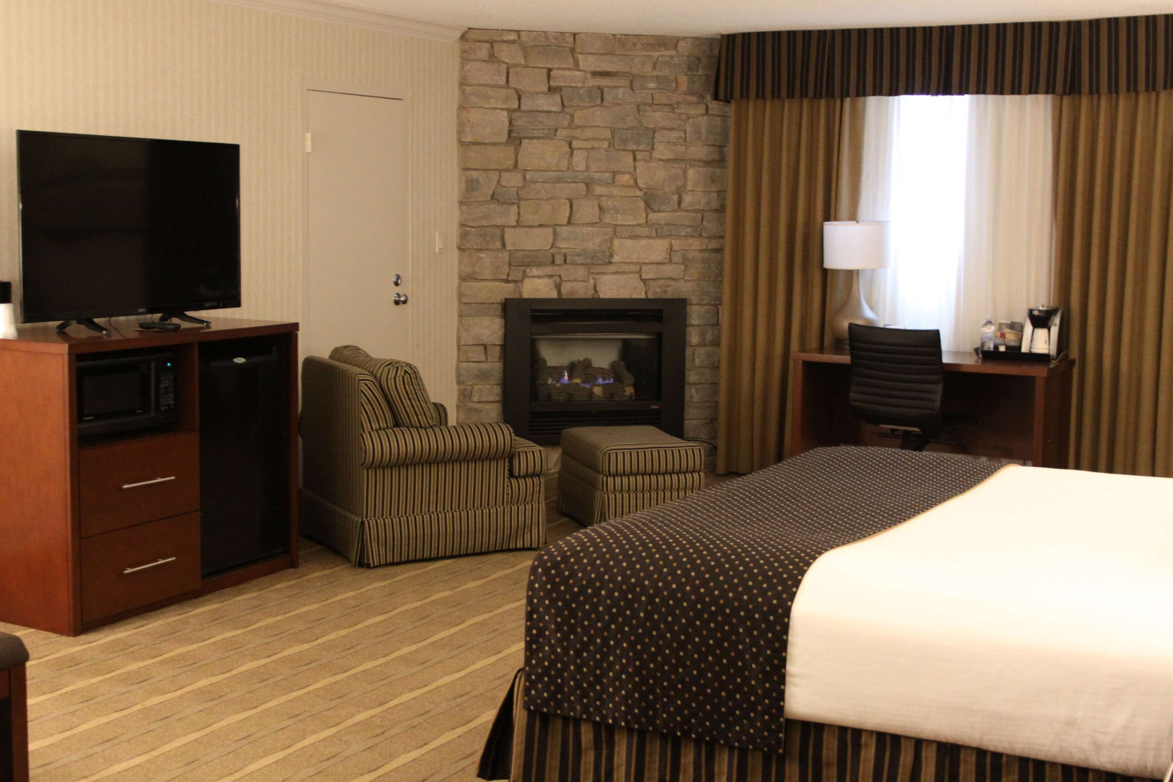 A hotel room with a bed, a television, a fireplace, a desk, and a chair.