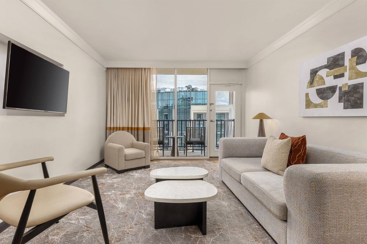 A modern living room with a flat-screen TV, two round coffee tables, a sofa, and a chair.
