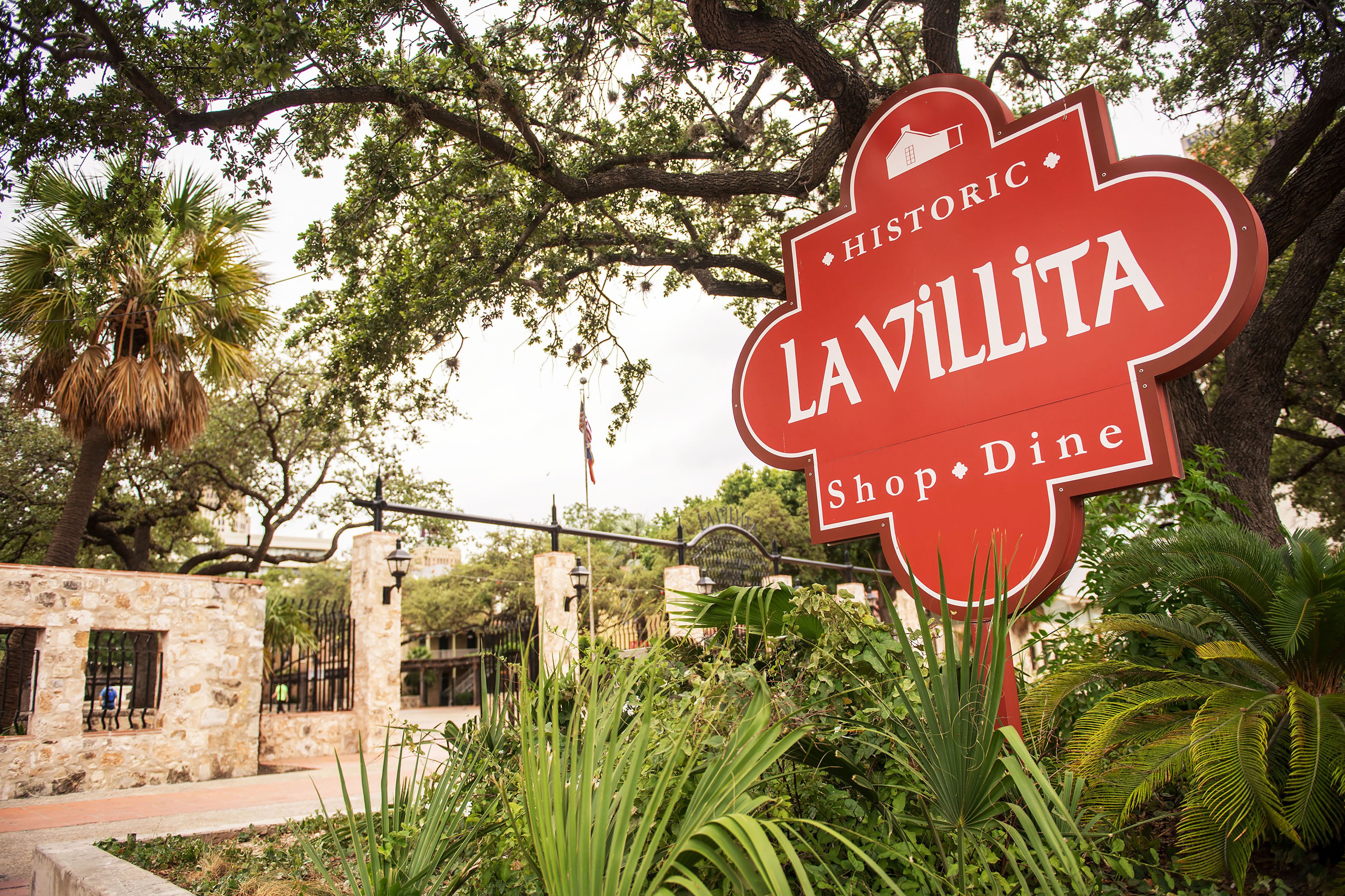 Un panneau historique indiquant l’emplacement de La Villita Shop & Dine, entouré d’une végétation luxuriante.