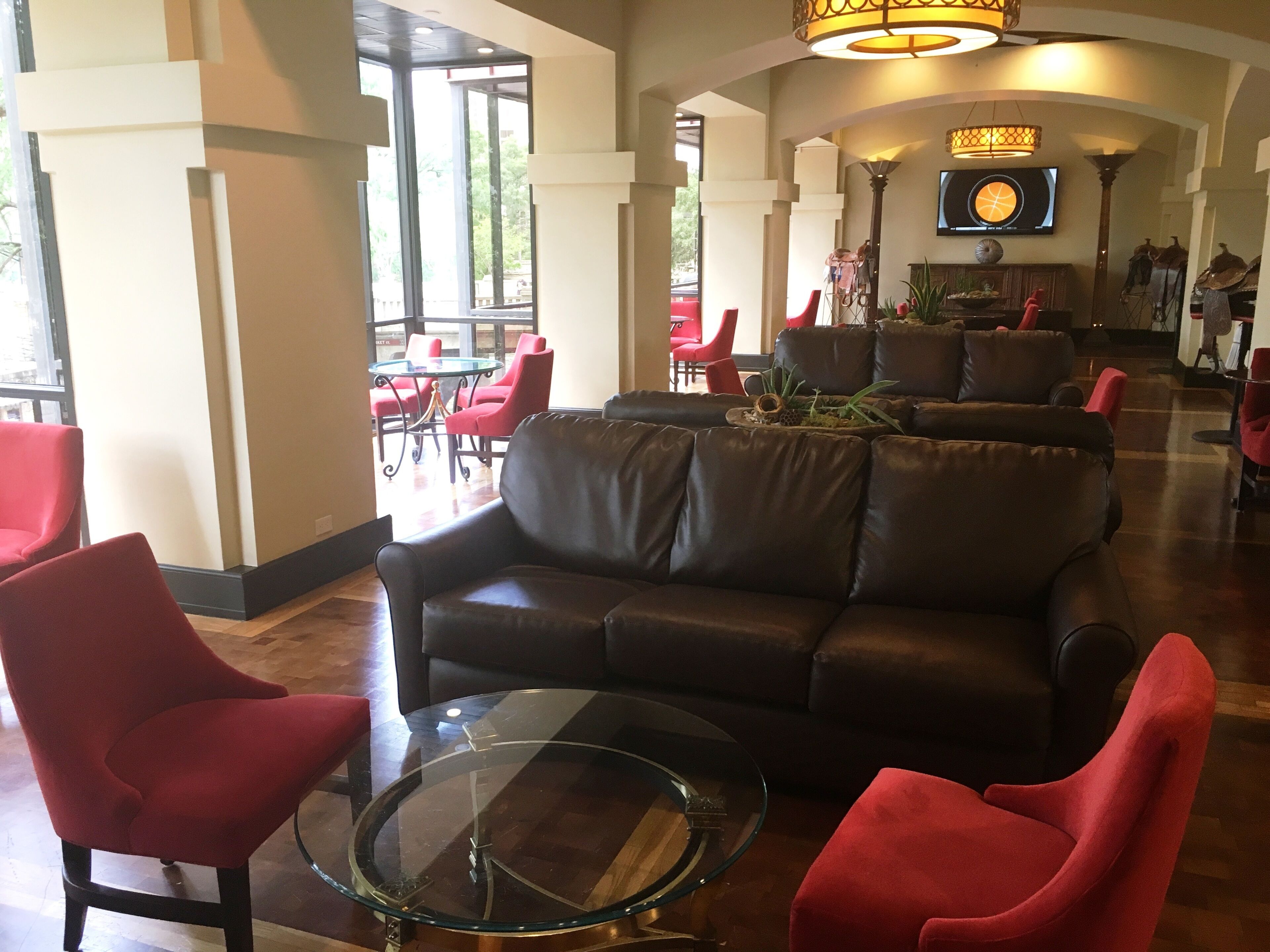 A lobby with a leather sofa, red chairs, a glass coffee table, and a TV mounted on the wall.
