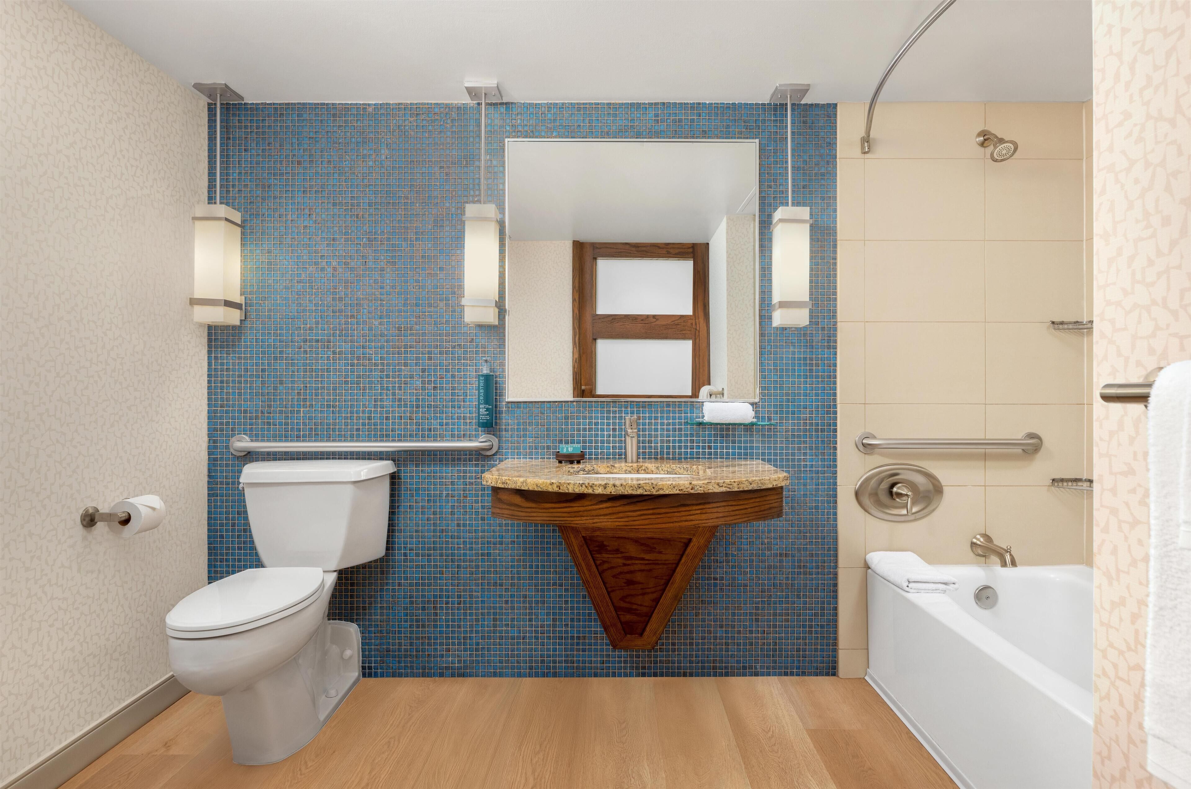 Un baño con pared de azulejos azules, tocador de madera, inodoro blanco, bañera y ducha.