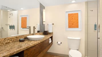 A modern bathroom with a granite countertop, a white sink, a large mirror, and a toilet.