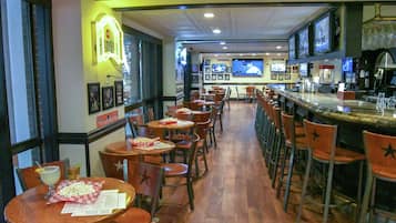 Un restaurante con varias mesas y sillas, una zona de bar y un letrero de neón en la pared.