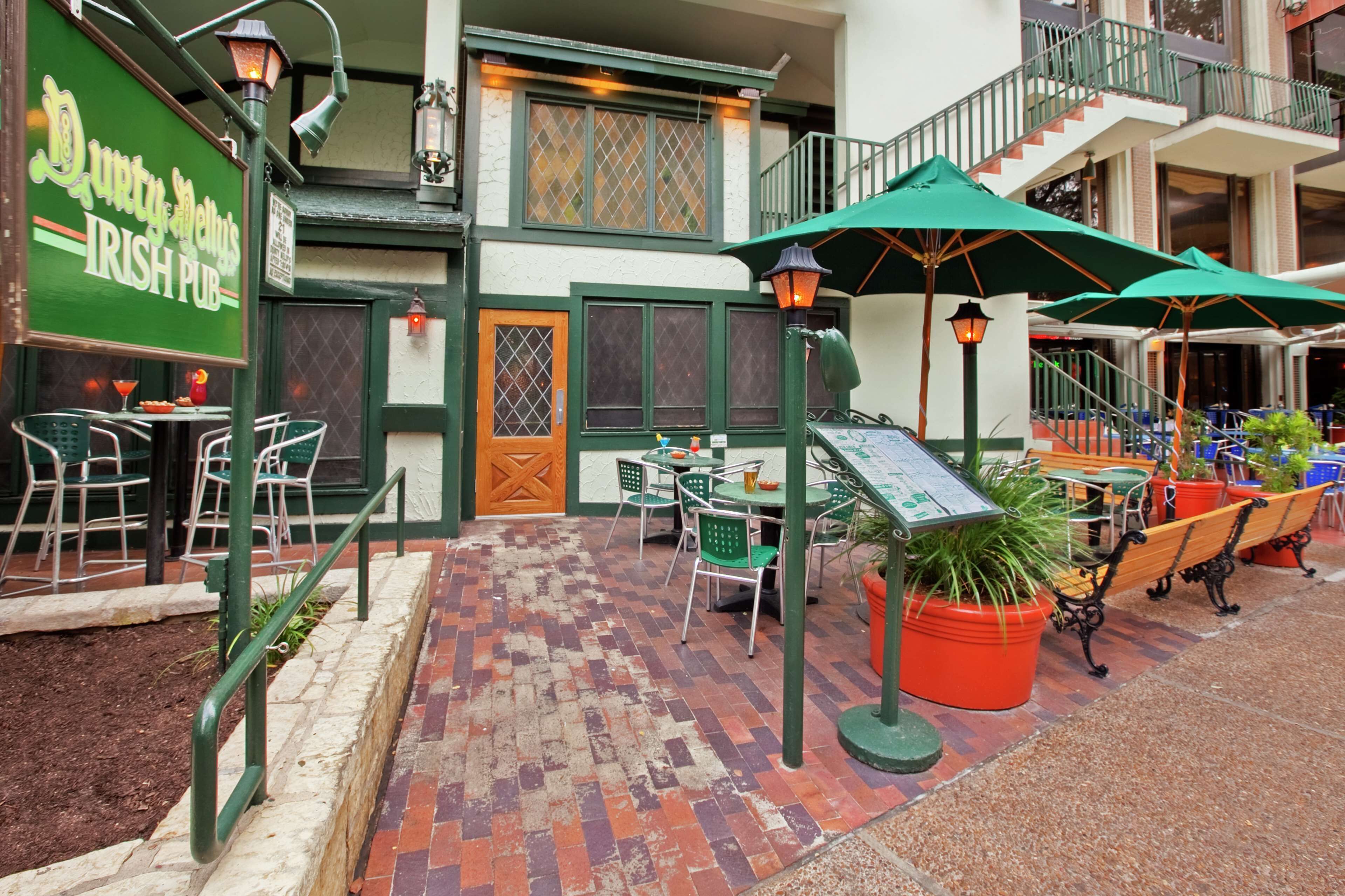 Un área de estar al aire libre acogedora, con sillas y mesas verdes, un letrero que dice 'Durty Mettle Irish Pub' y una escalera que conduce a un nivel superior.