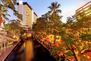 A riverside hotel with outdoor seating and a bridge. - Hilton Palacio Del Rio (San Antonio)