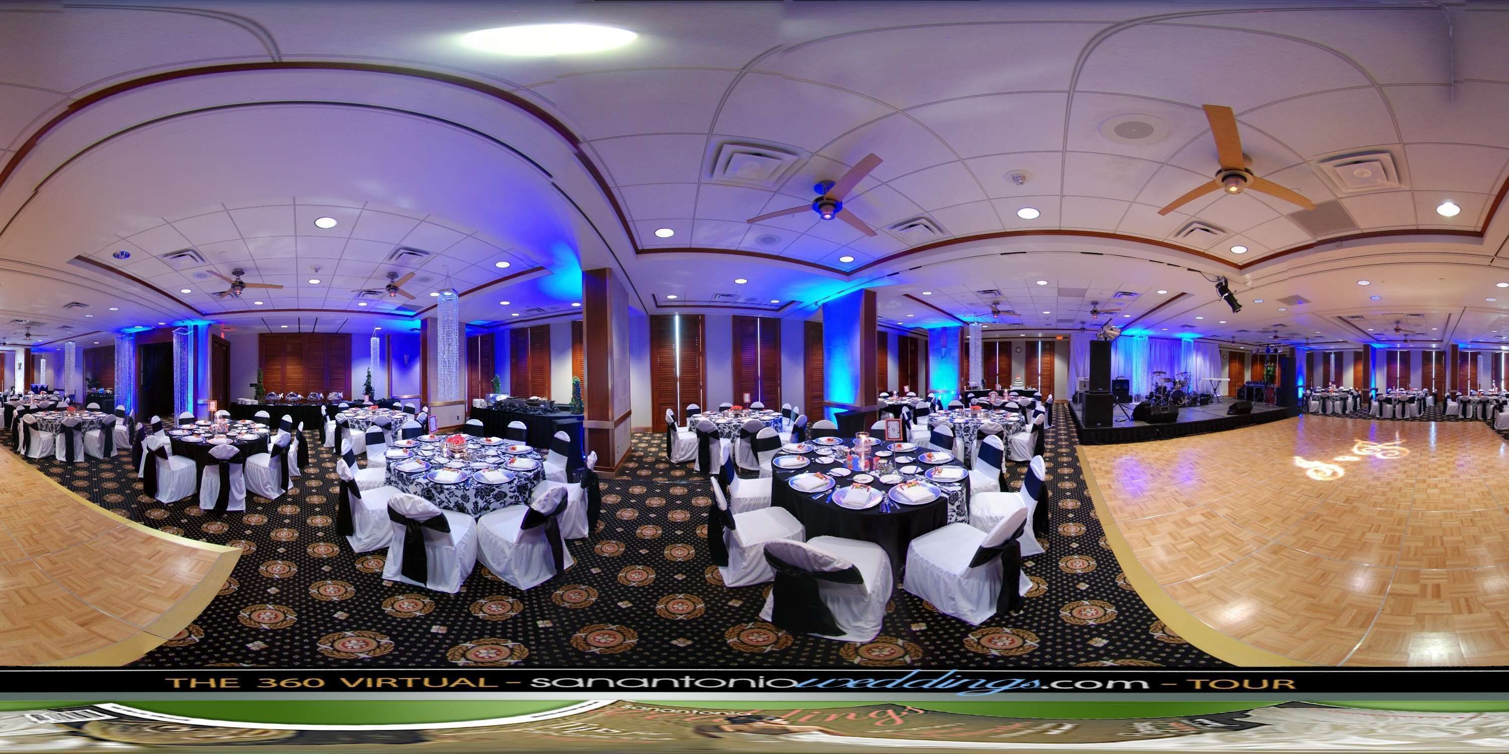 A large banquet hall with round tables, white tablecloths, and black chairs.