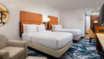 A hotel room with two beds, a desk, a chair, and a patterned carpet.