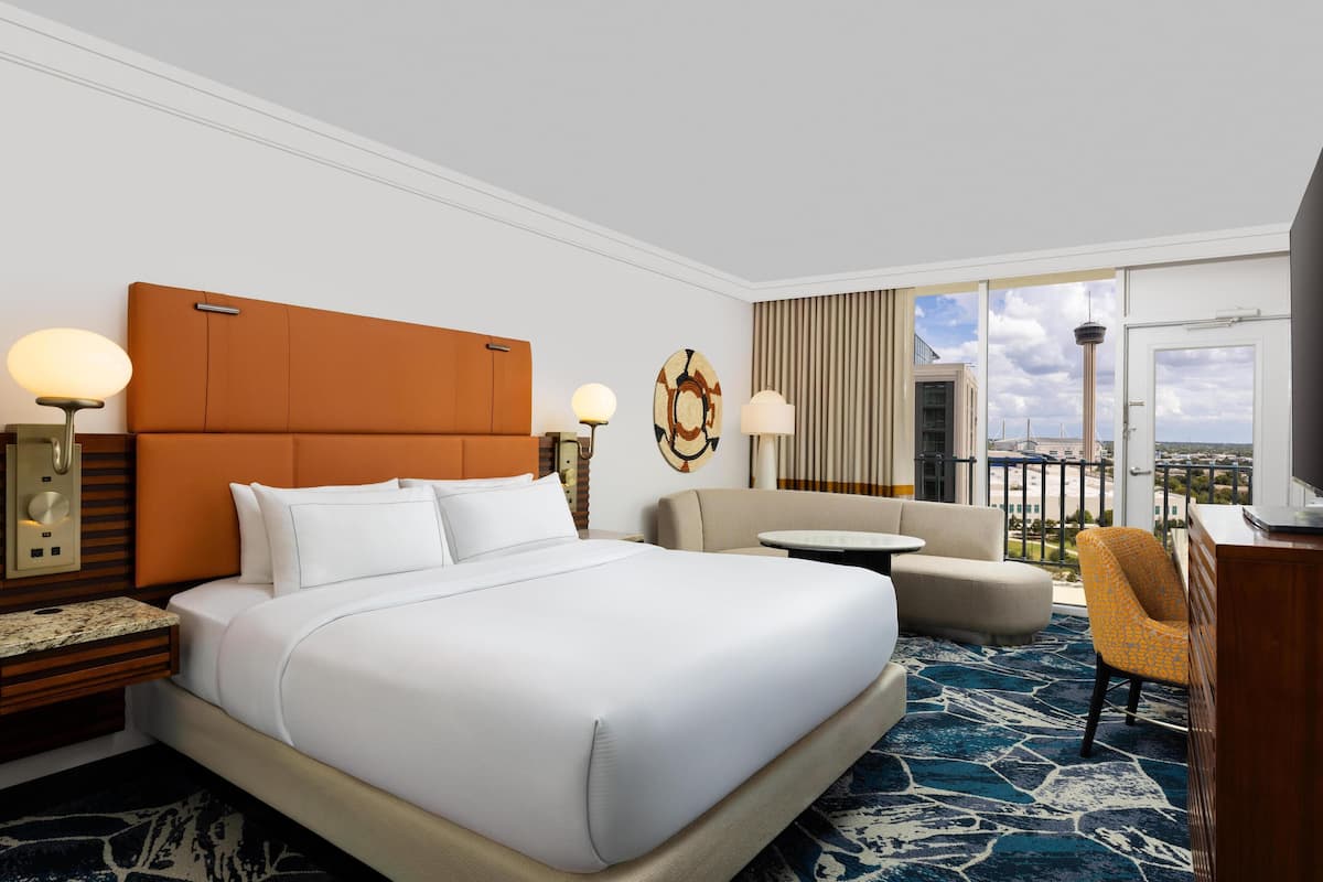 A hotel room with a large bed, a sofa, a small table, and a TV.