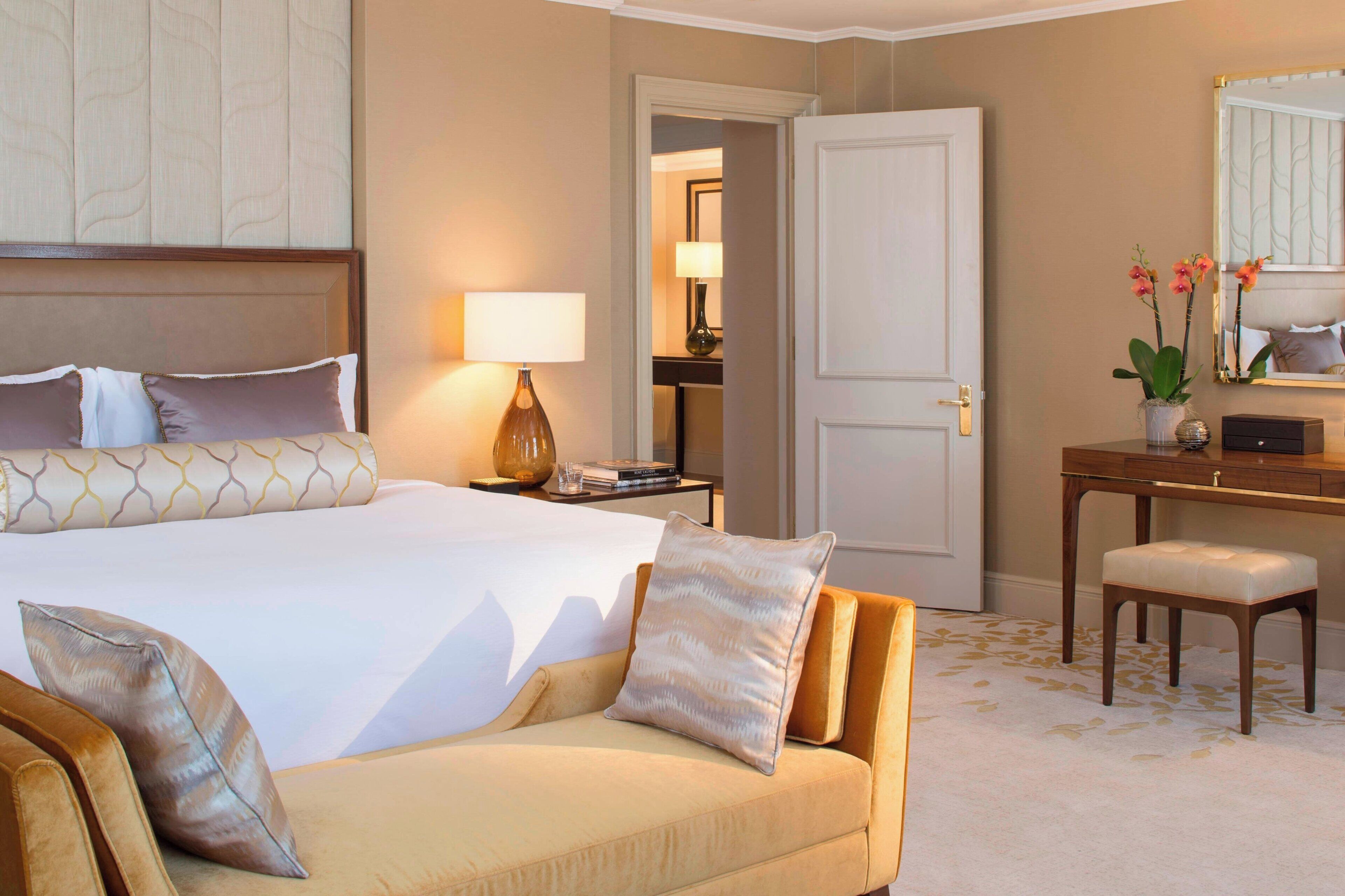 A hotel room with a large bed, a sofa, a desk, and a mirror.