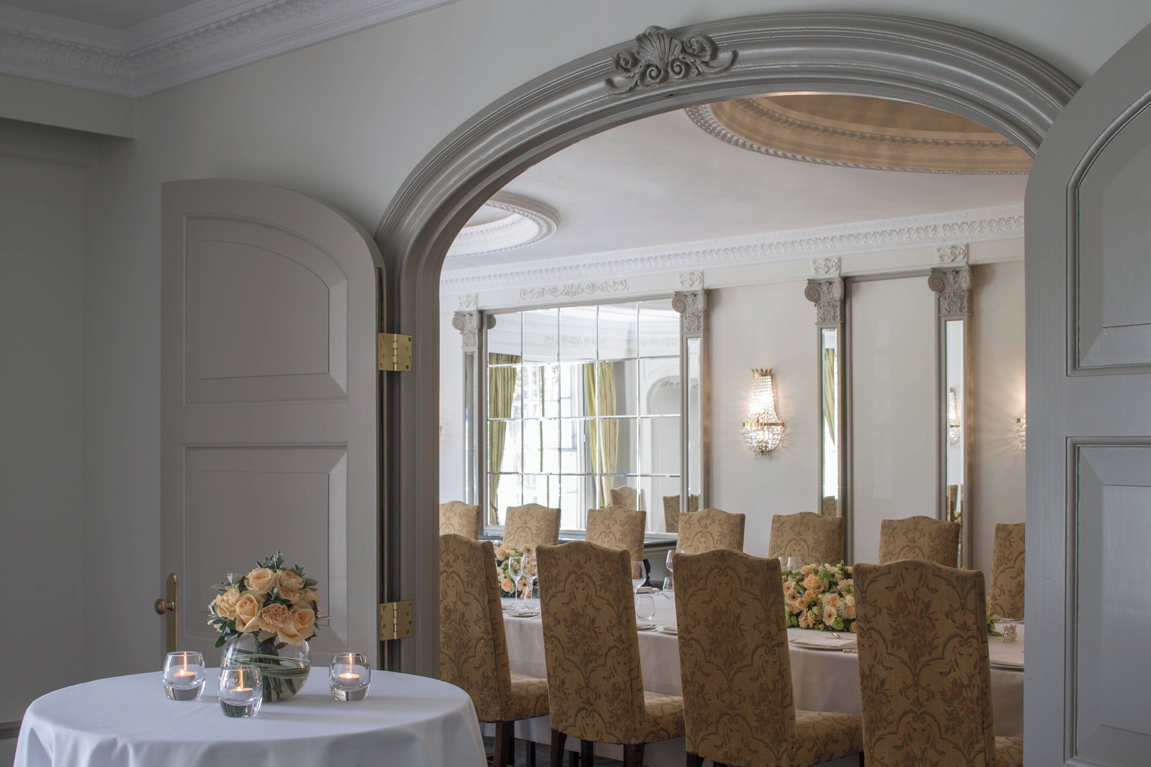A formal dining room with a round table, chairs, and a vase of flowers.