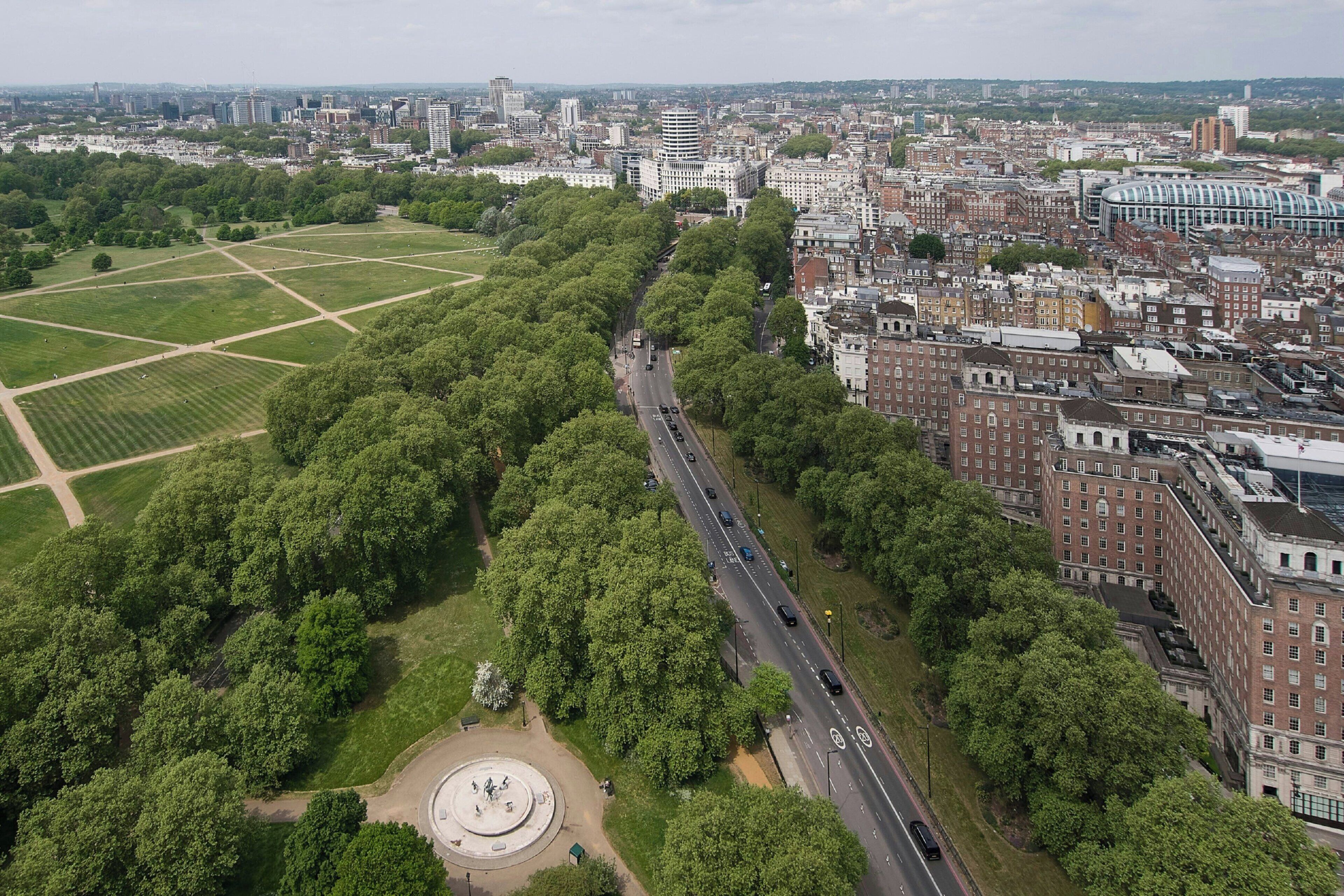 An aerial view of a city with a large green park, a central road, and surrounding buildings.