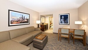 Een hotelkamer met een bank, voetenbankje, een bureau met stoel, een spiegel en twee ingelijste foto's aan de muur.
