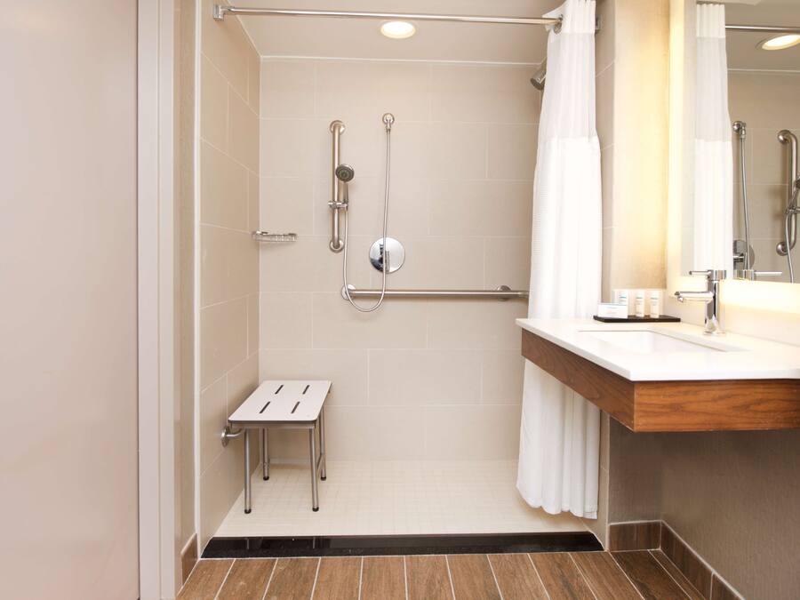 Un baño moderno con cabina de ducha, barra de apoyo y un taburete pequeño.