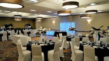 A banquet hall with round tables, white chairs, and black tablecloths.