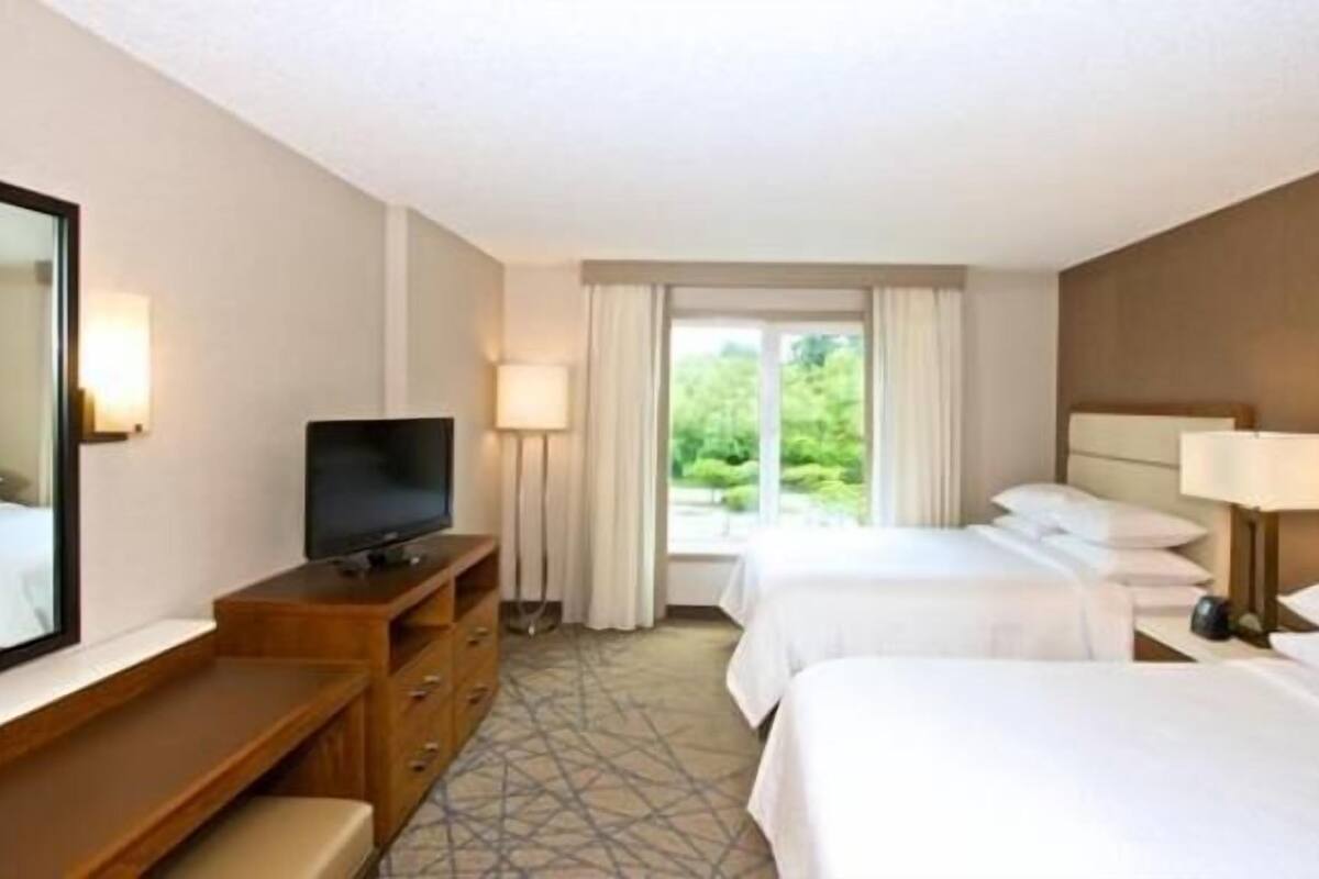 Een hotelkamer met twee bedden, een televisie, een bureau en een grote spiegel.