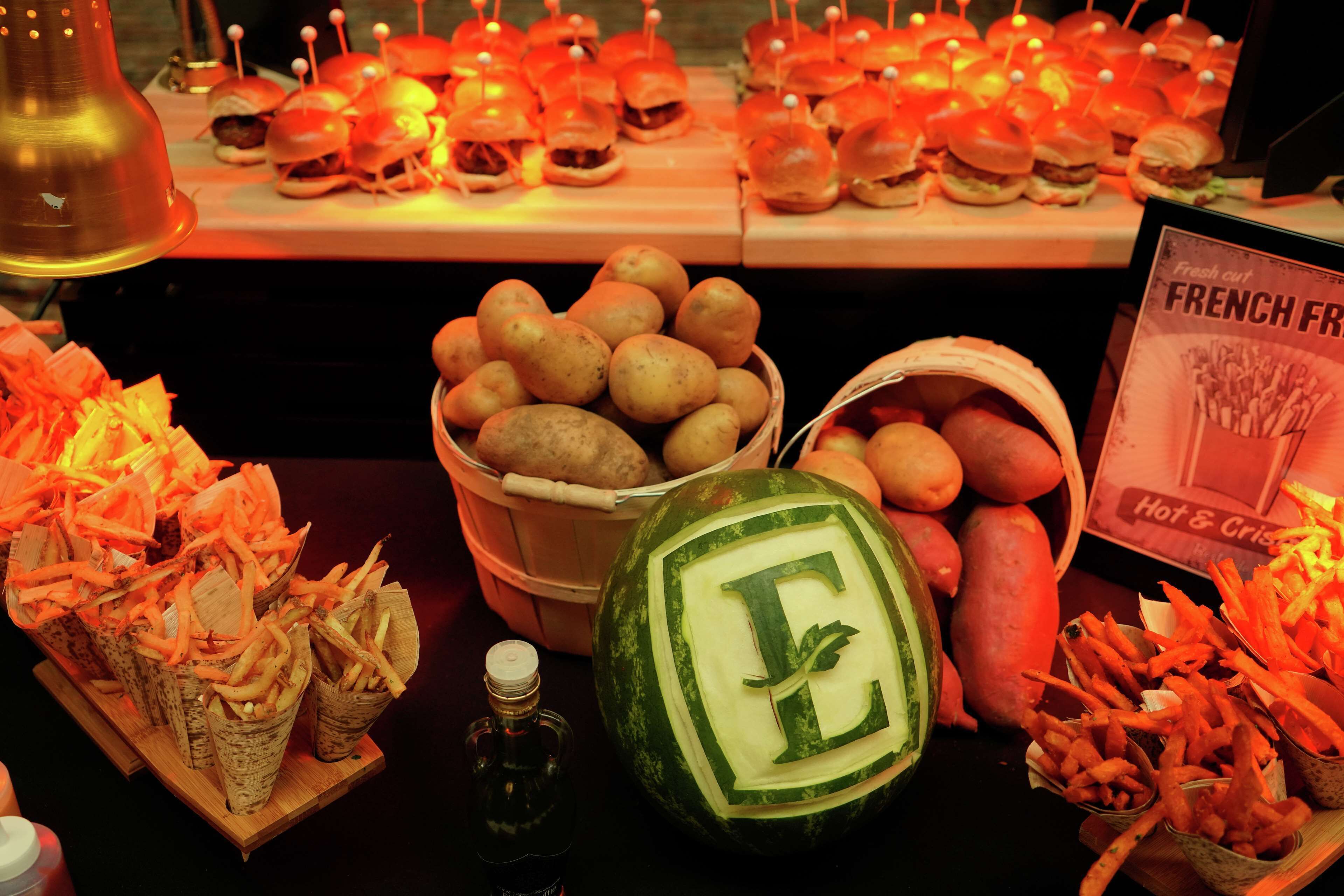 Una mesa de buffet con diferentes opciones de comida, incluyendo una sandía tallada, cestas de papas y patatas fritas.