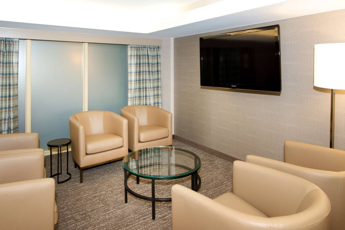 Een hotelkamer met een zithoek, bestaande uit twee leren fauteuils, een glazen salontafel en een wandgemonteerde flatscreen televisie.