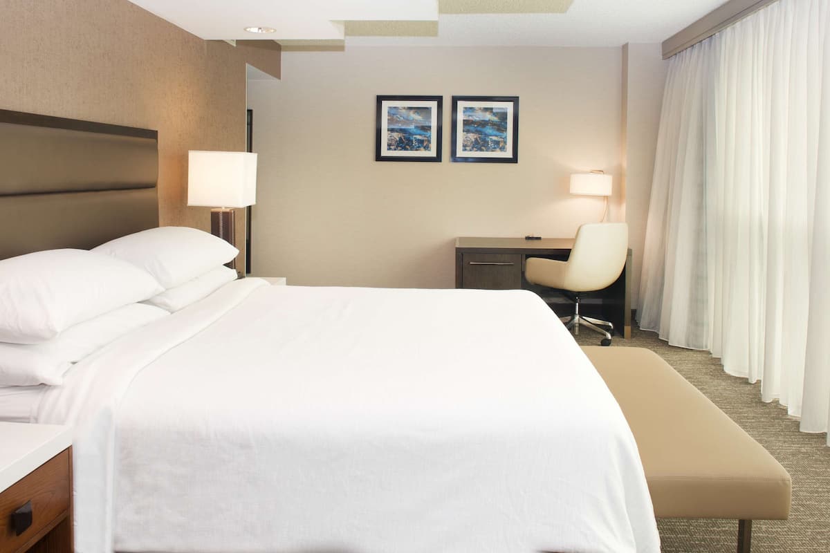 Een hotelkamer met een groot bed, een bureau, een stoel en een raam met gordijnen.