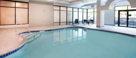 An indoor swimming pool with clear water, tiled edges, and a pool ladder.