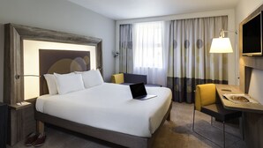 A hotel room with a large bed, a desk with a chair, a laptop, and a TV.