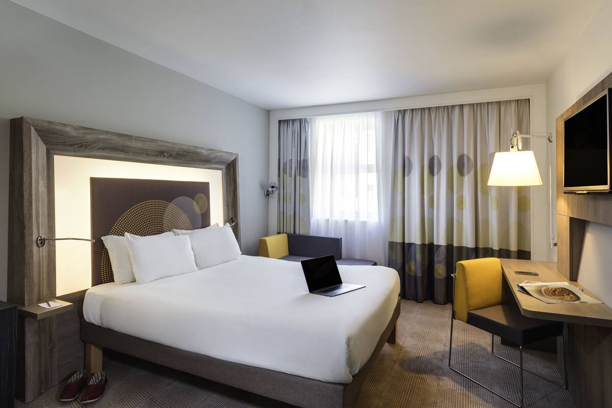 A hotel room with a large bed, a desk with a chair, a laptop, and a TV.
