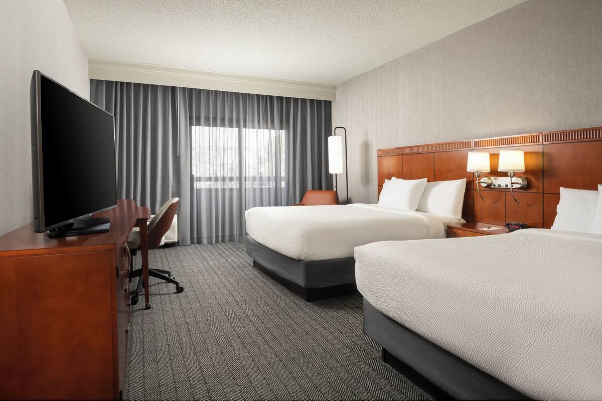 A hotel room with two beds, a desk, a television, and a lamp.